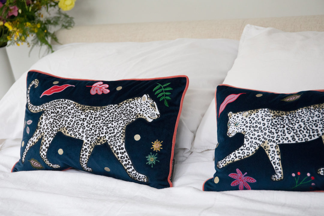 Leopard Bolster Cushion, navy blue velvet with white snow leopard embroidery surrounded by leaf motifs, edged with pink contrast velvet trim